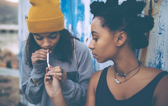 Teenage girl helps her friend light a cigarette.